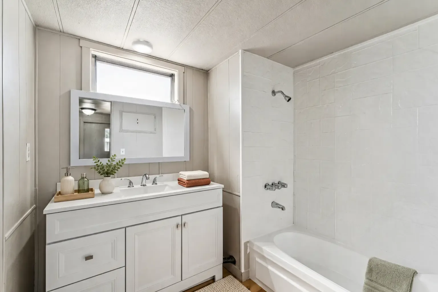 Baño con tocador blanco, espejo con marco, ventana y tina con azulejo alrededor de la regadera