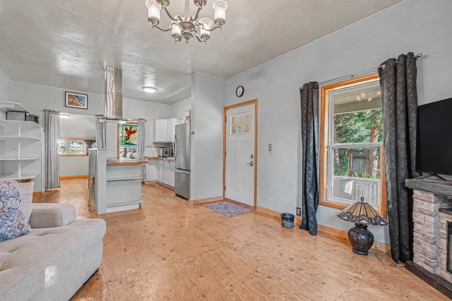 Open living area looking toward the kitchen with a breakfast bar, stainless-steel refrigerator and wood plank flooring