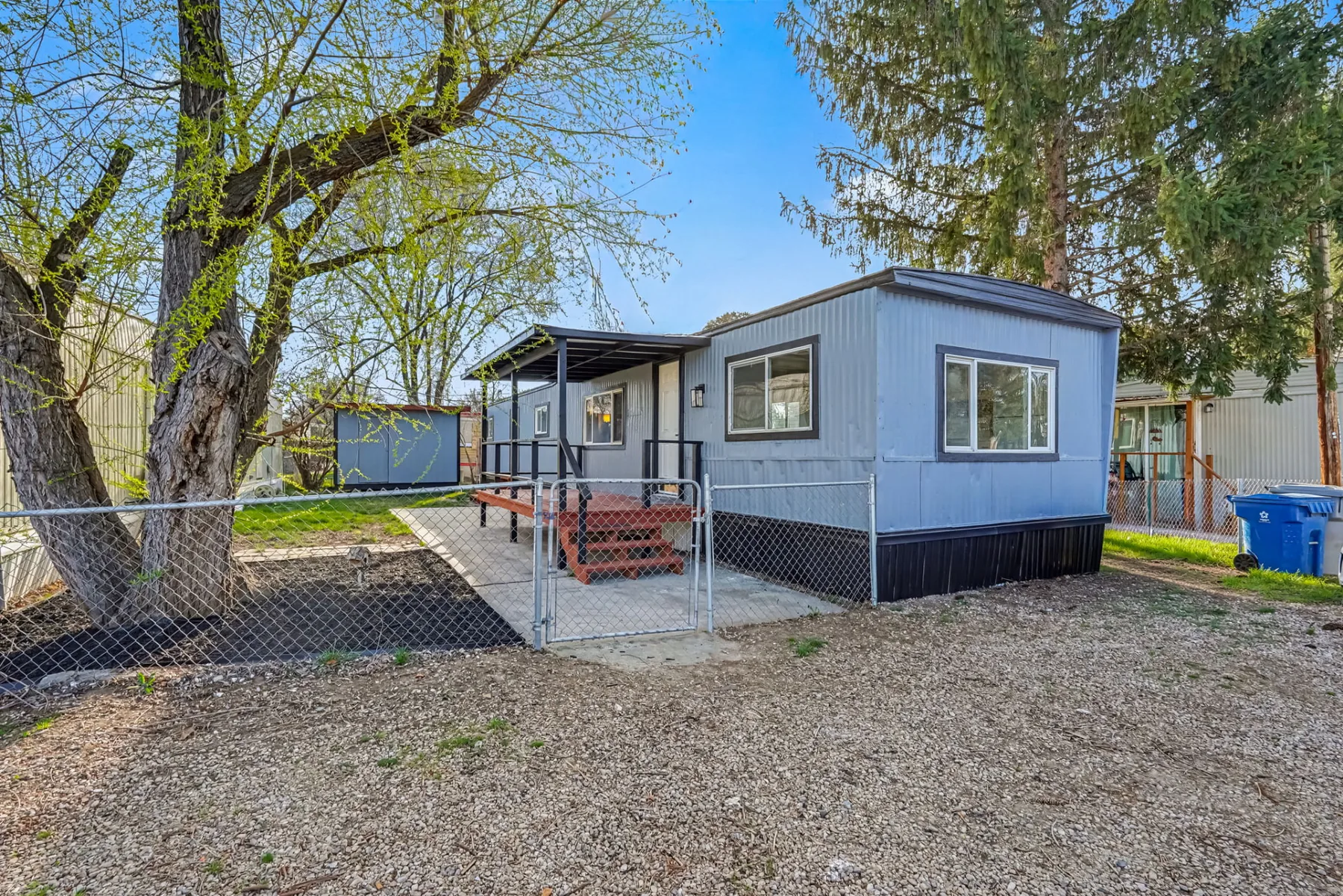 Front exterior of 415 E 44th St Unit 9 in Garden City, Idaho, a single-level manufactured home with a covered entry, steps and a chain-link fenced yard