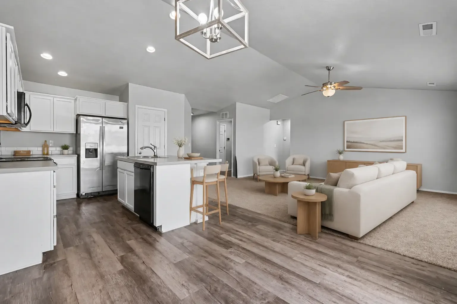 Kitchen with white cabinetry, center island with breakfast bar and sink, stainless-steel refrigerator and vinyl plank flooring open to the living area