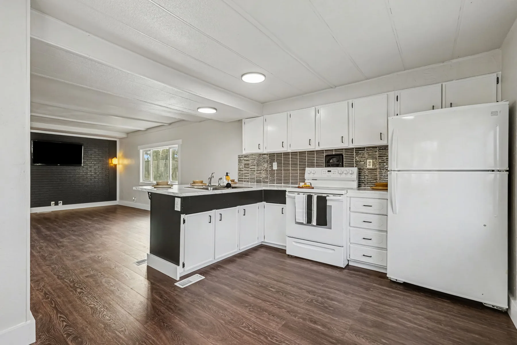 Kitchen with white cabinetry, breakfast bar, range, refrigerator and tile backsplash, open to the living area