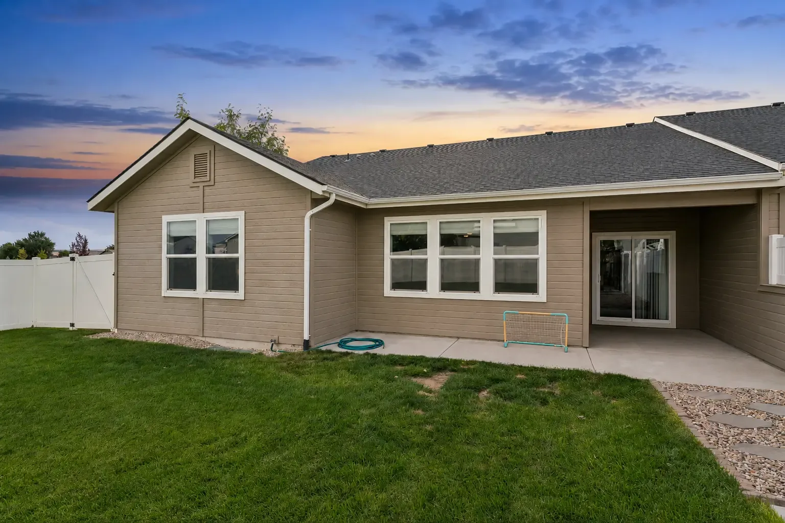 Rear exterior at dusk showing the covered patio, concrete area, lawn and white vinyl privacy fence