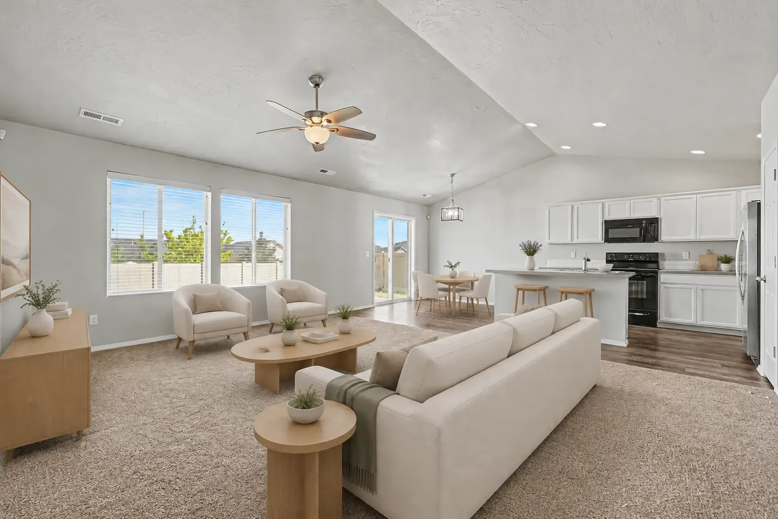 Open great room with carpeted living area, dining space by the patio slider and the kitchen with breakfast bar beyond