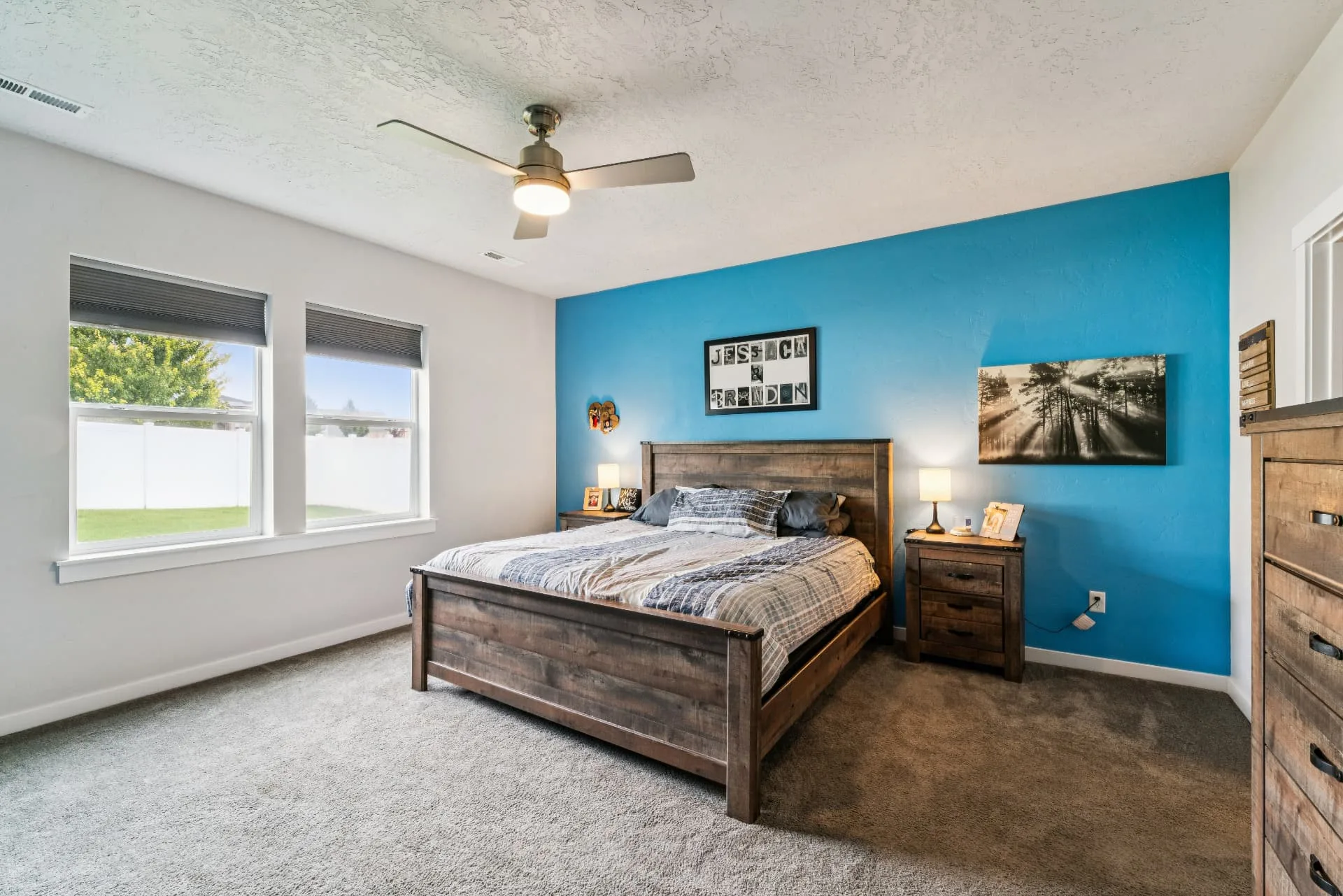 Primary bedroom with carpet, ceiling fan, two windows and a painted blue accent wall