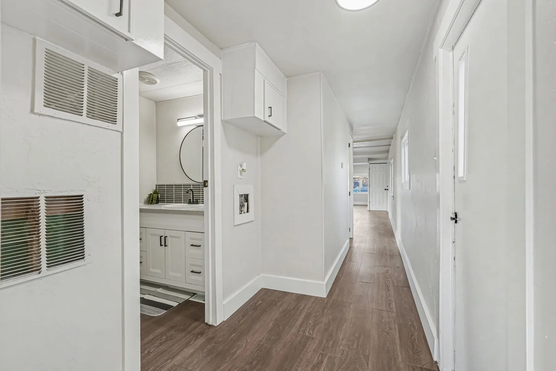 Hallway with wood-look flooring, built-in cabinetry and a view into the bathroom vanity area
