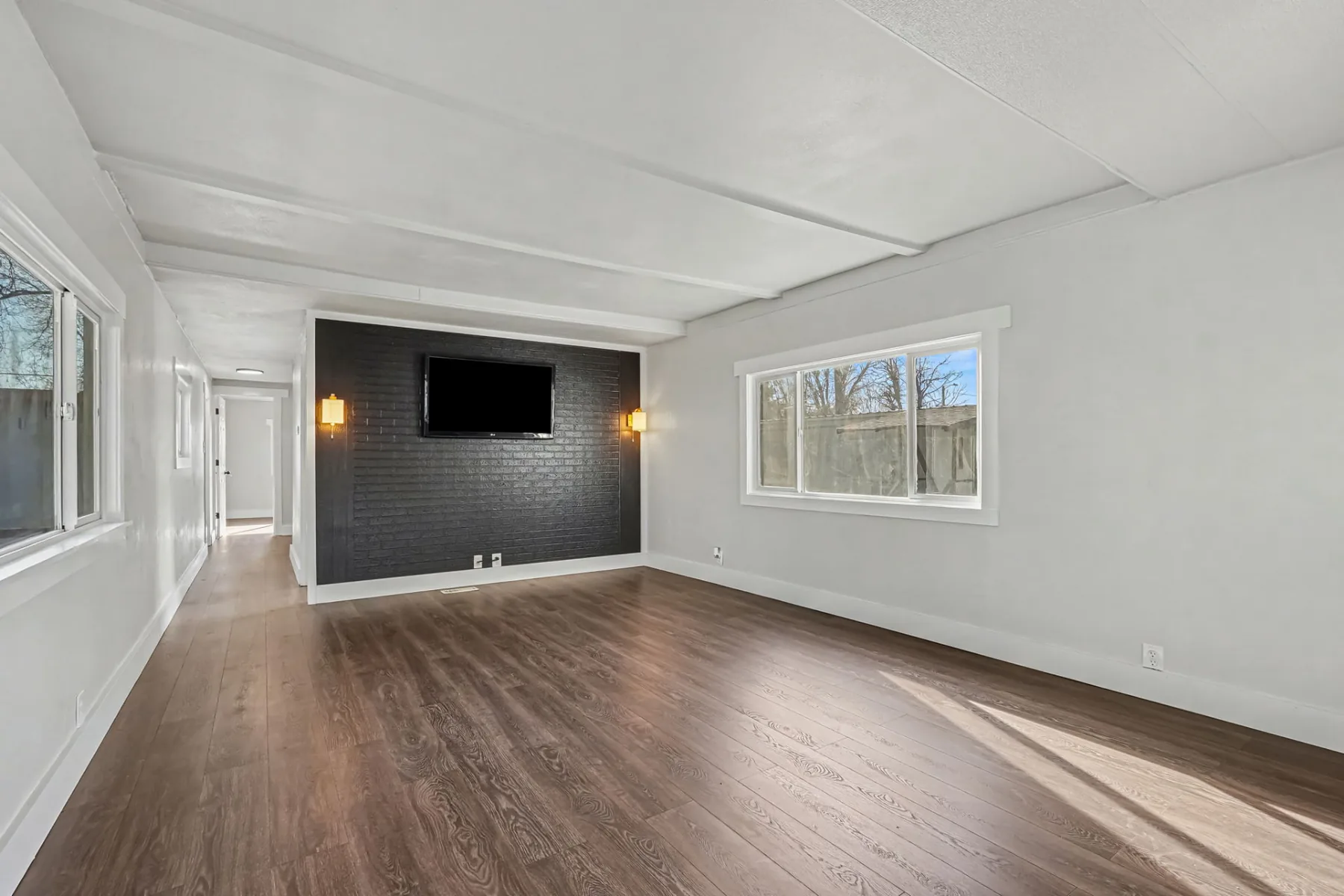 Living area with wood-look plank flooring, a dark accent wall, wall sconces and a window
