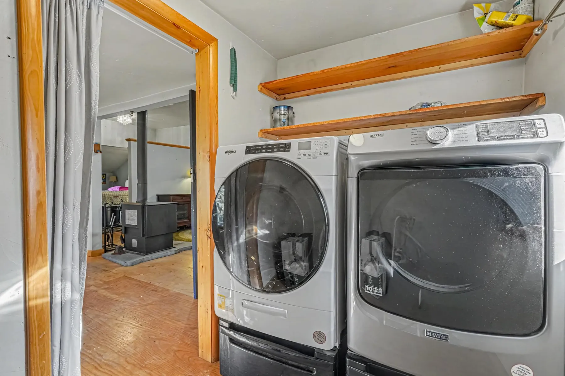 Laundry area with a front-load washer and dryer, wood shelving and a view toward the wood stove