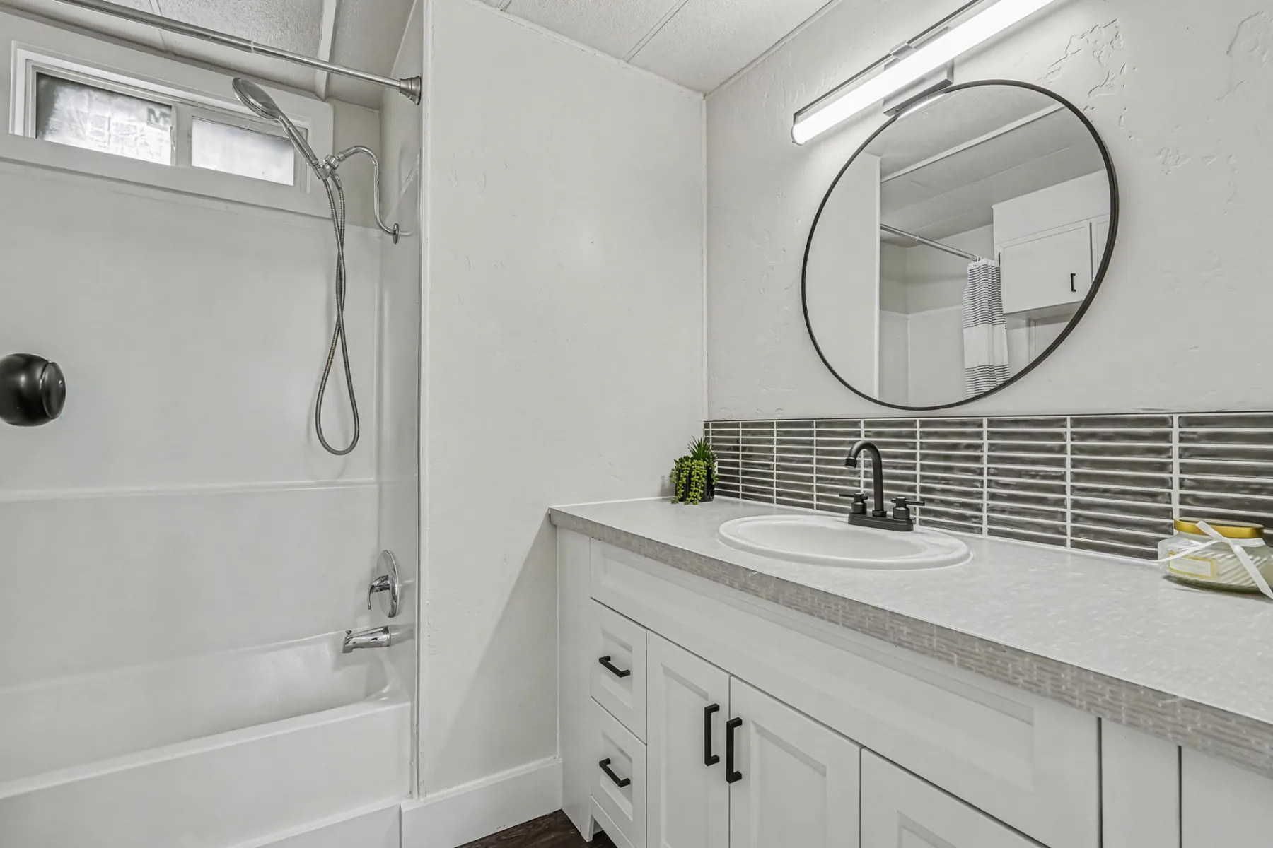 Bathroom with a tub and shower, vanity with a round mirror and tile backsplash