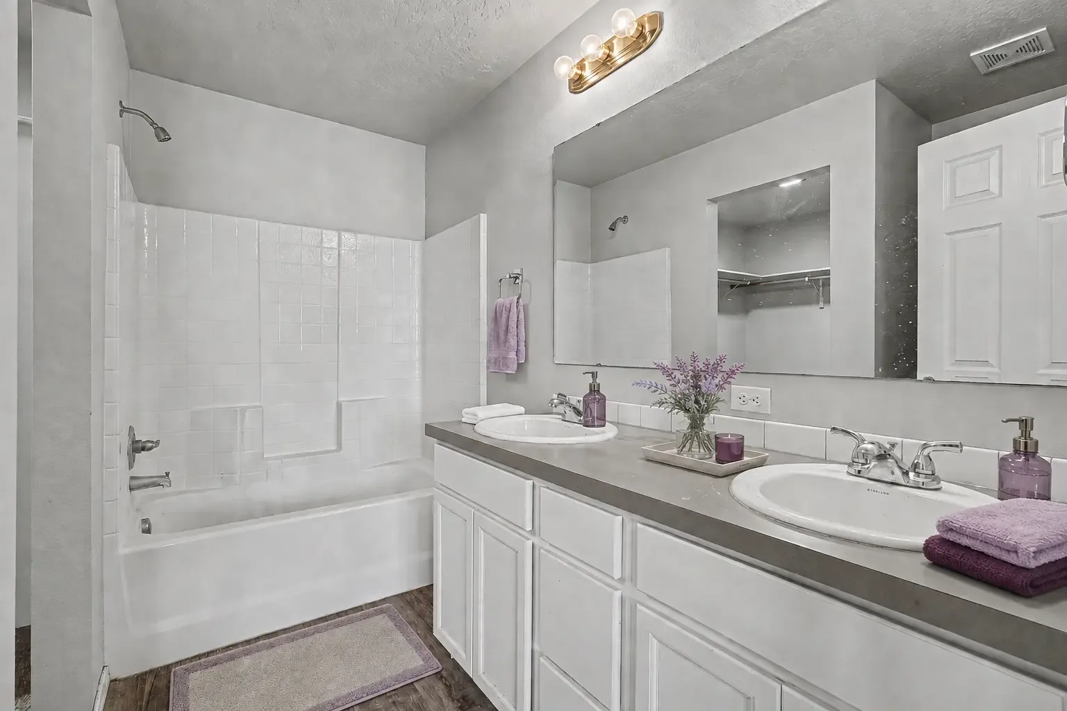 Primary bathroom with a dual-sink vanity, large mirror and a tub with tiled surround