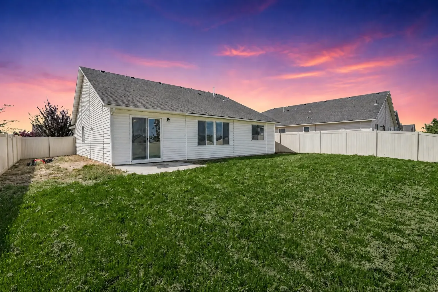 Rear exterior at dusk showing the back of the home, patio slab and sliding glass door with a vinyl-fenced yard