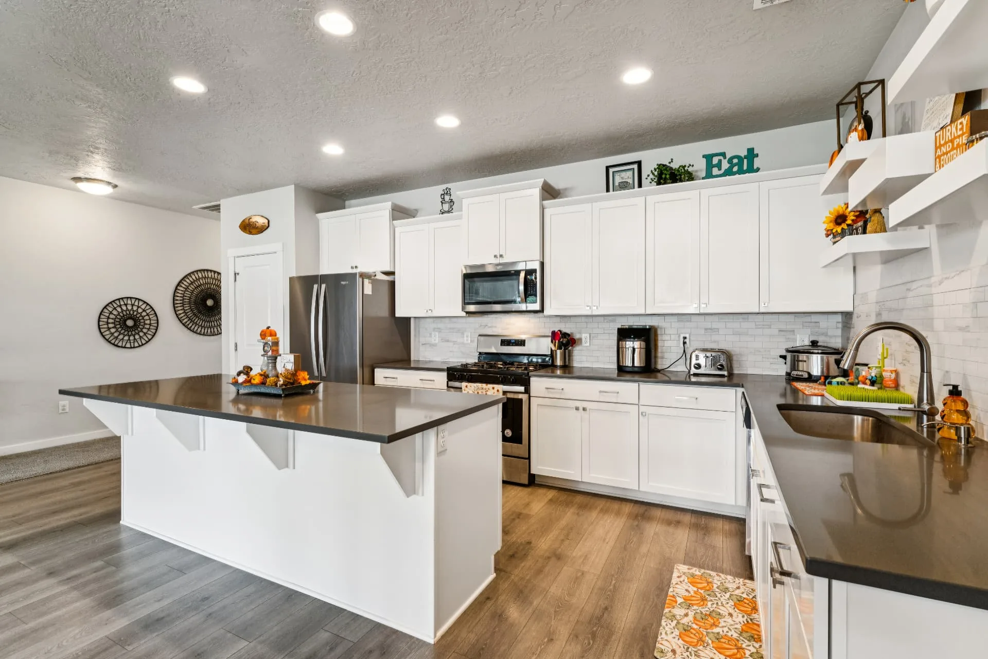 Kitchen with white cabinetry, center island with breakfast bar, dark counters, tile backsplash and stainless-steel appliances