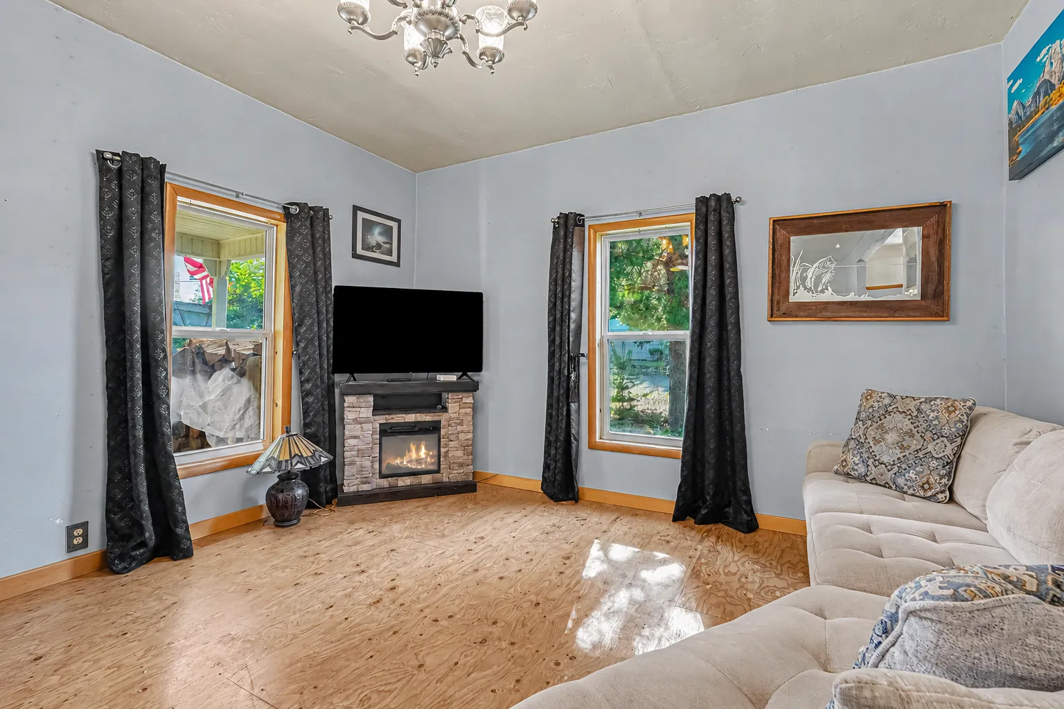 Living room with two curtained windows, a stone-front fireplace and a sofa